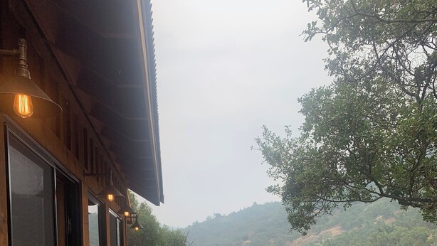 A wooden deck with a table and chairs, overlooking a river and hills.