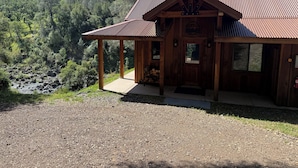 A wooden cabin with a metal roof, a porch, and a view of a forested valley.