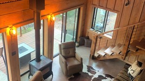 A cozy interior with a fireplace, comfortable seating, and large windows offering views of the outdoors.
