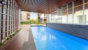 Une piscine intérieure moderne dotée d’un plafond en lambris de bois, de murs en verre et d’un sol carrelé.