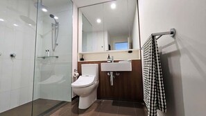 Un baño moderno con cabina de ducha de vidrio, inodoro, lavabo con espejo y toallero.