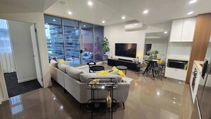 Un salon moderne avec un canapé, une table basse et un téléviseur. Il y a un balcon avec vue sur les immeubles.