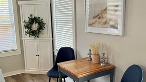 Un coin repas avec une table en bois et deux chaises, un meuble blanc orné d’une guirlande, et un tableau encadré accroché au mur.