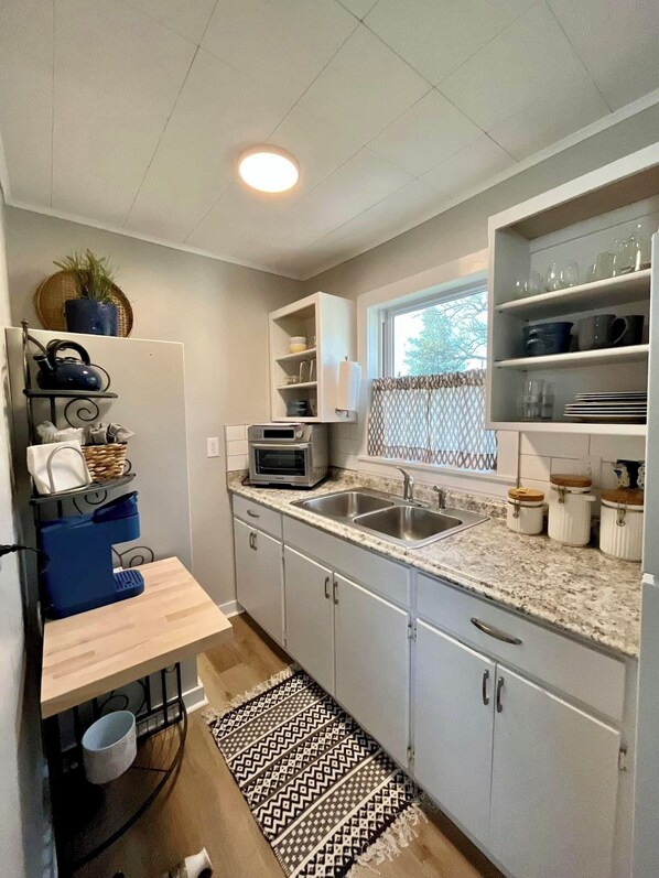 A compact kitchen with a built-in oven, a microwave, a sink, and a window with a view of greenery. - Cape Cod Style on Grand Lake - Romantic Honeymoon Cottage w/ Hot tub #11 (Grove)