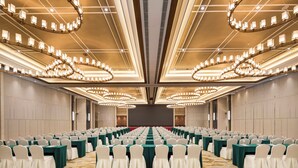 Un salón de conferencias con filas de mesas, sillas y una pantalla grande al frente.