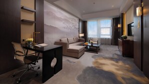 Una habitación de hotel moderna con sofá, escritorio y un ventanal grande.