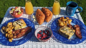 A breakfast setting with croissants, bacon, eggs, and fruit on a table. - Cottage On the Bay - Queen, Jetted tub, Full Kitchen, water view (Sequim)
