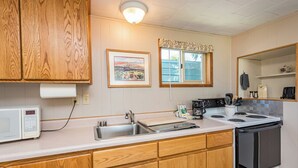 A kitchen with wooden cabinets, a microwave, a sink, a stove, and a window with a curtain. - Cottage On the Bay - Queen, Jetted tub, Full Kitchen, water view (Sequim)