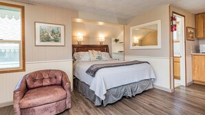 A bedroom with a bed, bedside lamps, a chair, a mirror, and a door leading to a kitchen. - Cottage On the Bay - Queen, Jetted tub, Full Kitchen, water view (Sequim)
