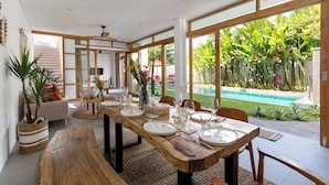 Comedor con mesa de madera para cuatro personas, ventanas amplias y vista a una piscina.