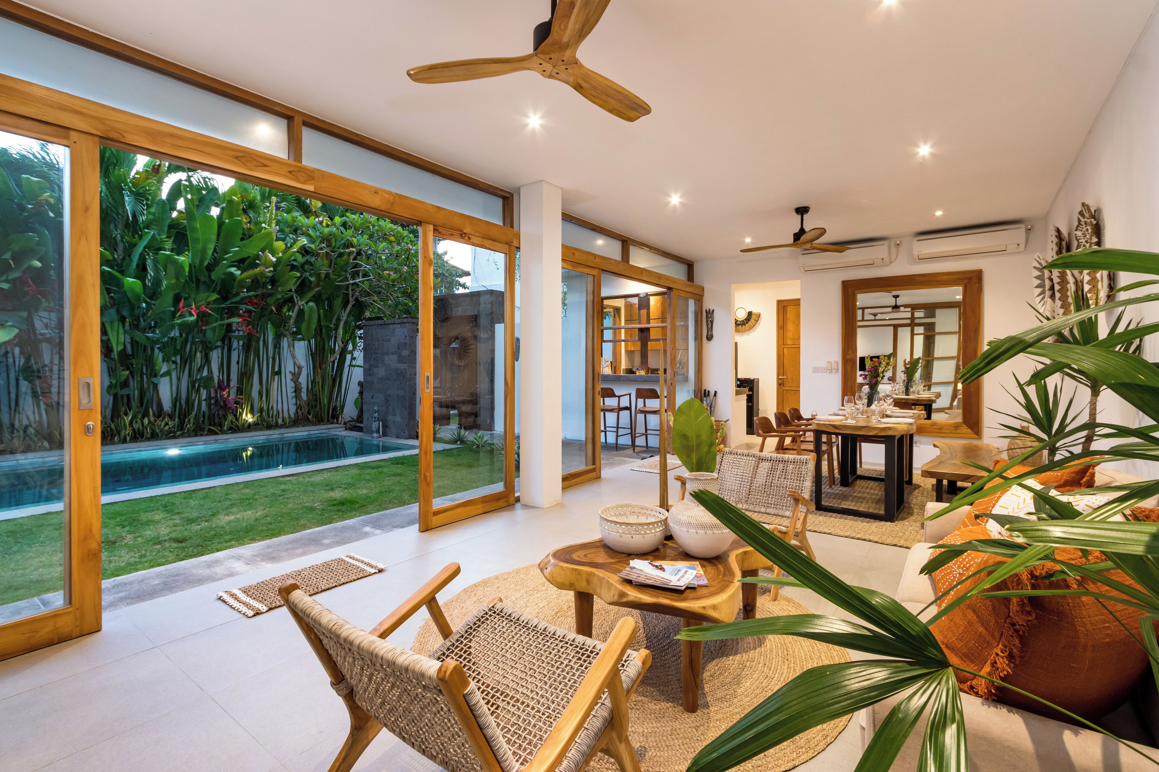 A spacious living area with a large glass door leading to a garden, a dining area with a table and chairs, and a ceiling fan.