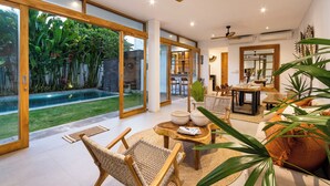 Amplia sala de estar con un gran ventanal que da a un jardín, un comedor con mesa y sillas, y un ventilador de techo.