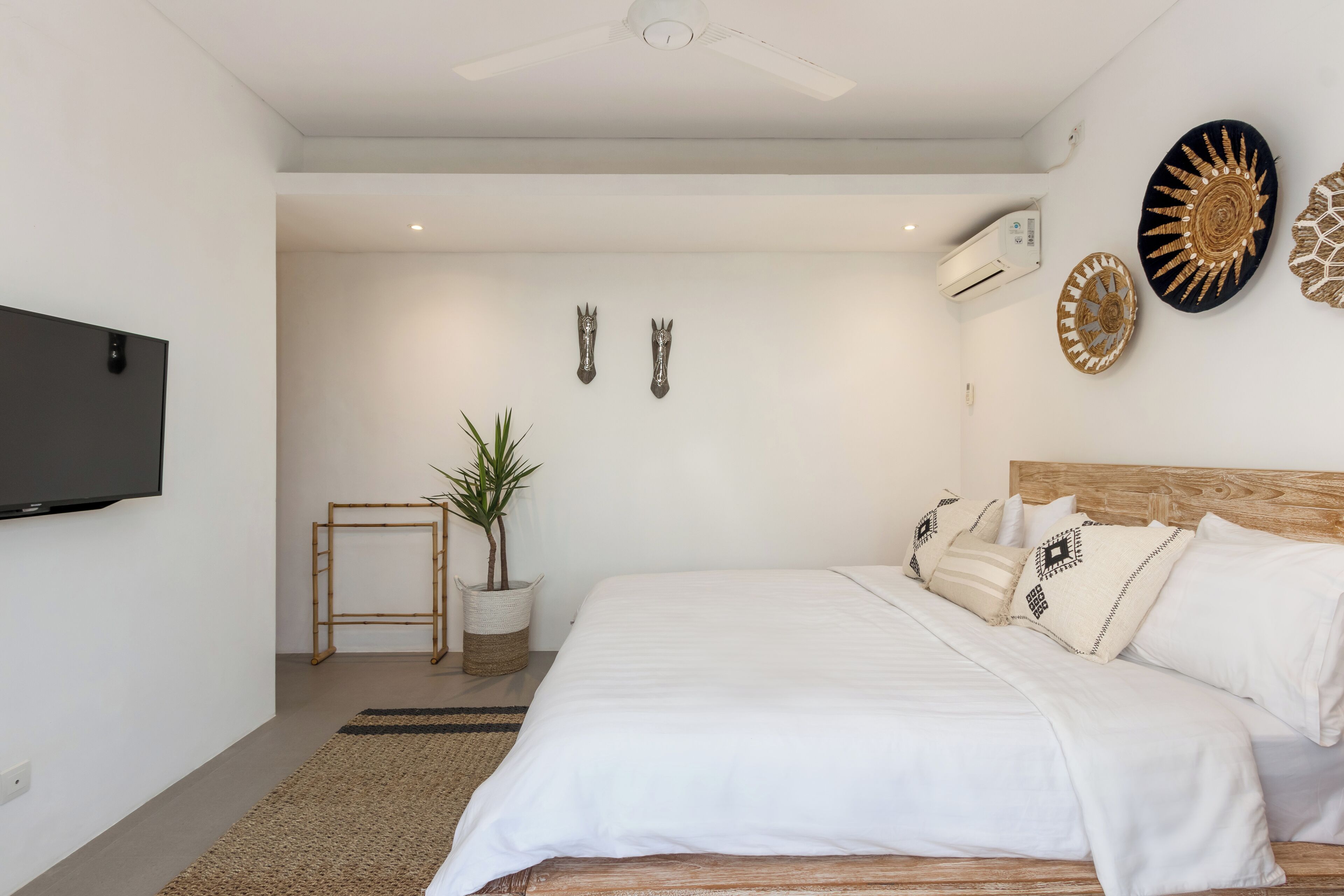 A modern bedroom with a large bed, a ceiling fan, a mounted TV, and decorative wall art.