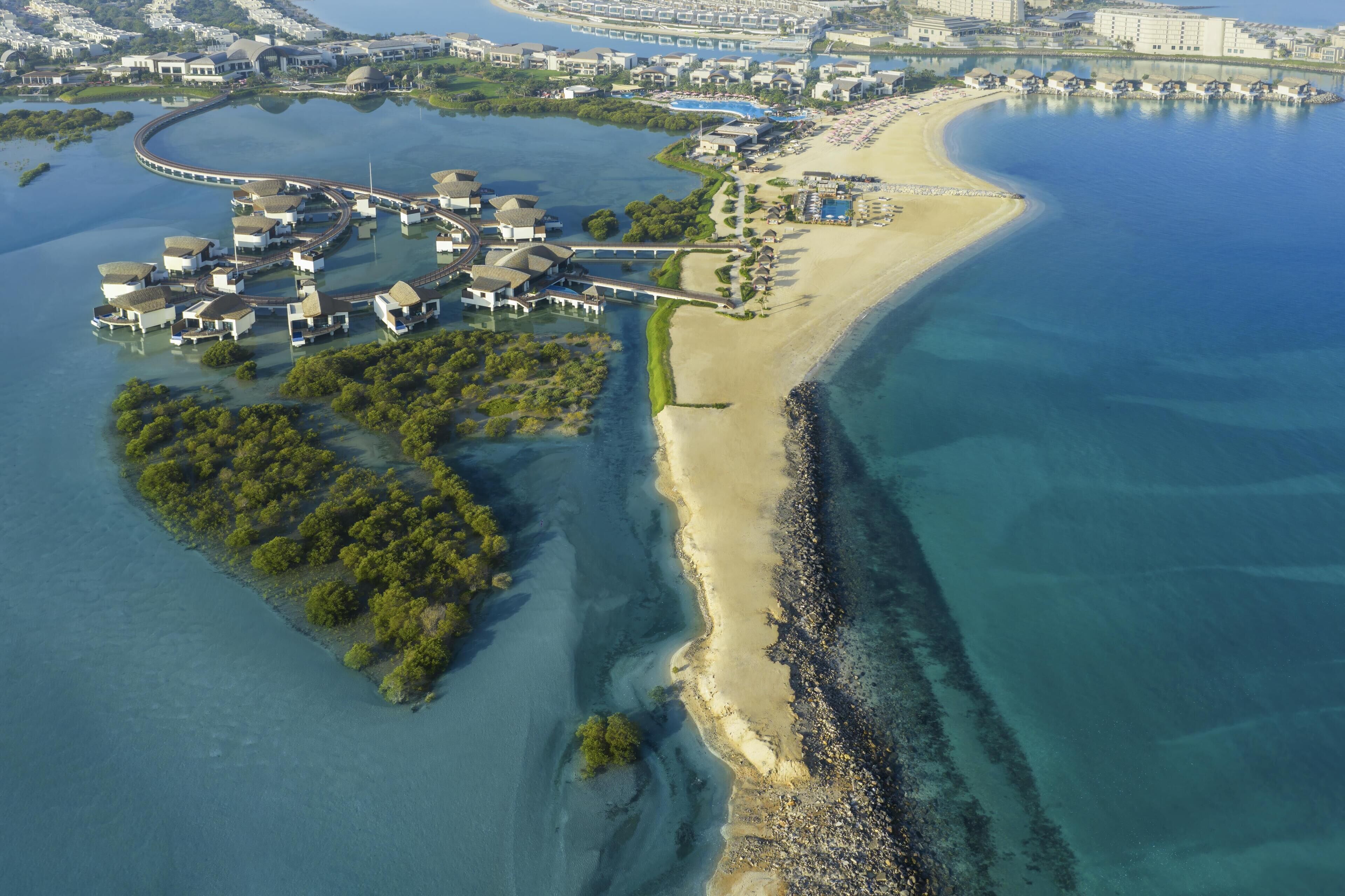 An aerial view of a coastal resort with villas, a beach, and a marina.