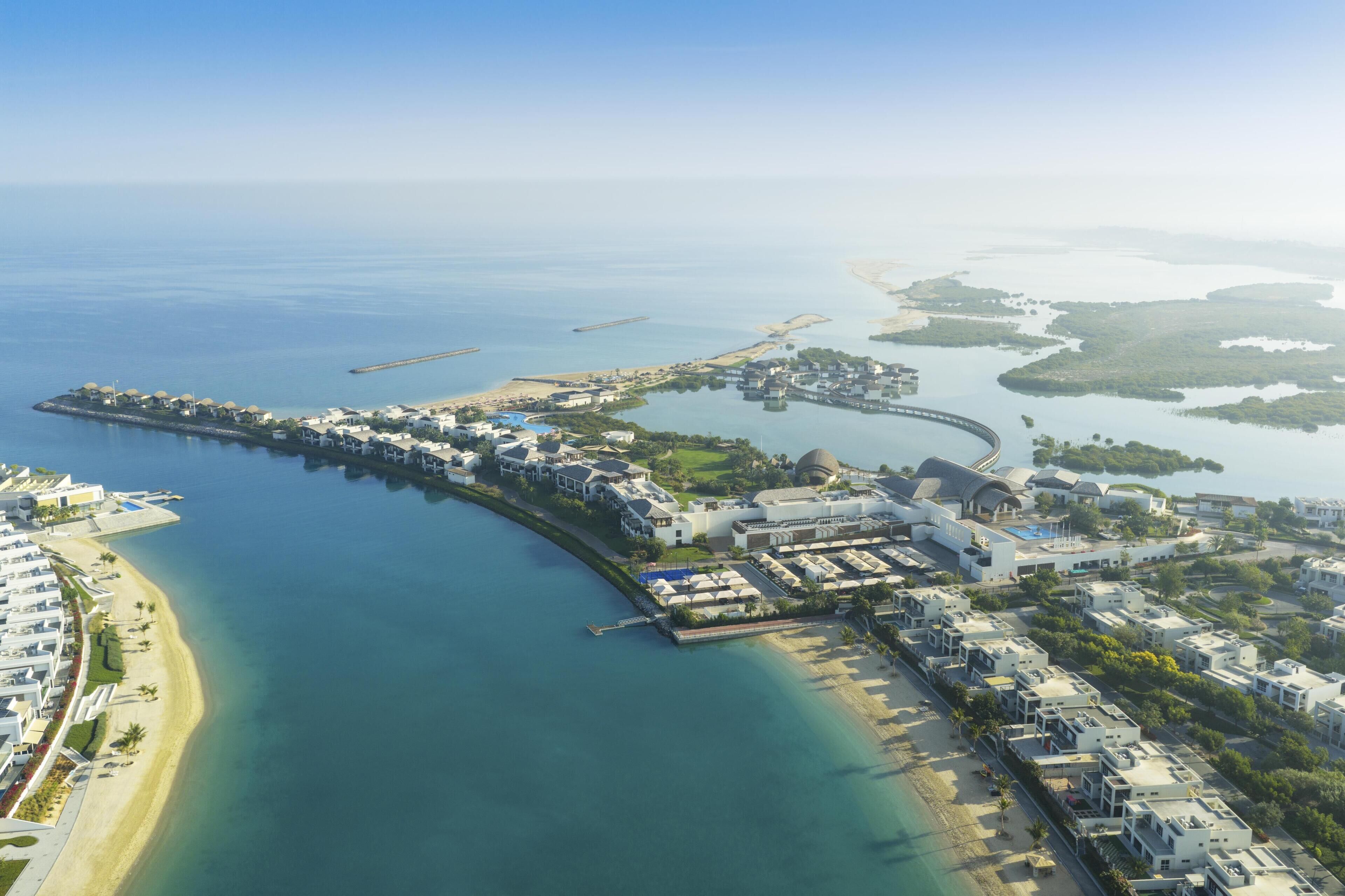 An aerial view of a coastal resort with a marina, beachfront villas, and a large building with a dome.