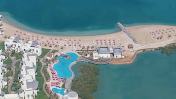 Ein Luftbild zeigt einen Ferienort mit großem Pool, Strand und mehreren Gebäuden.