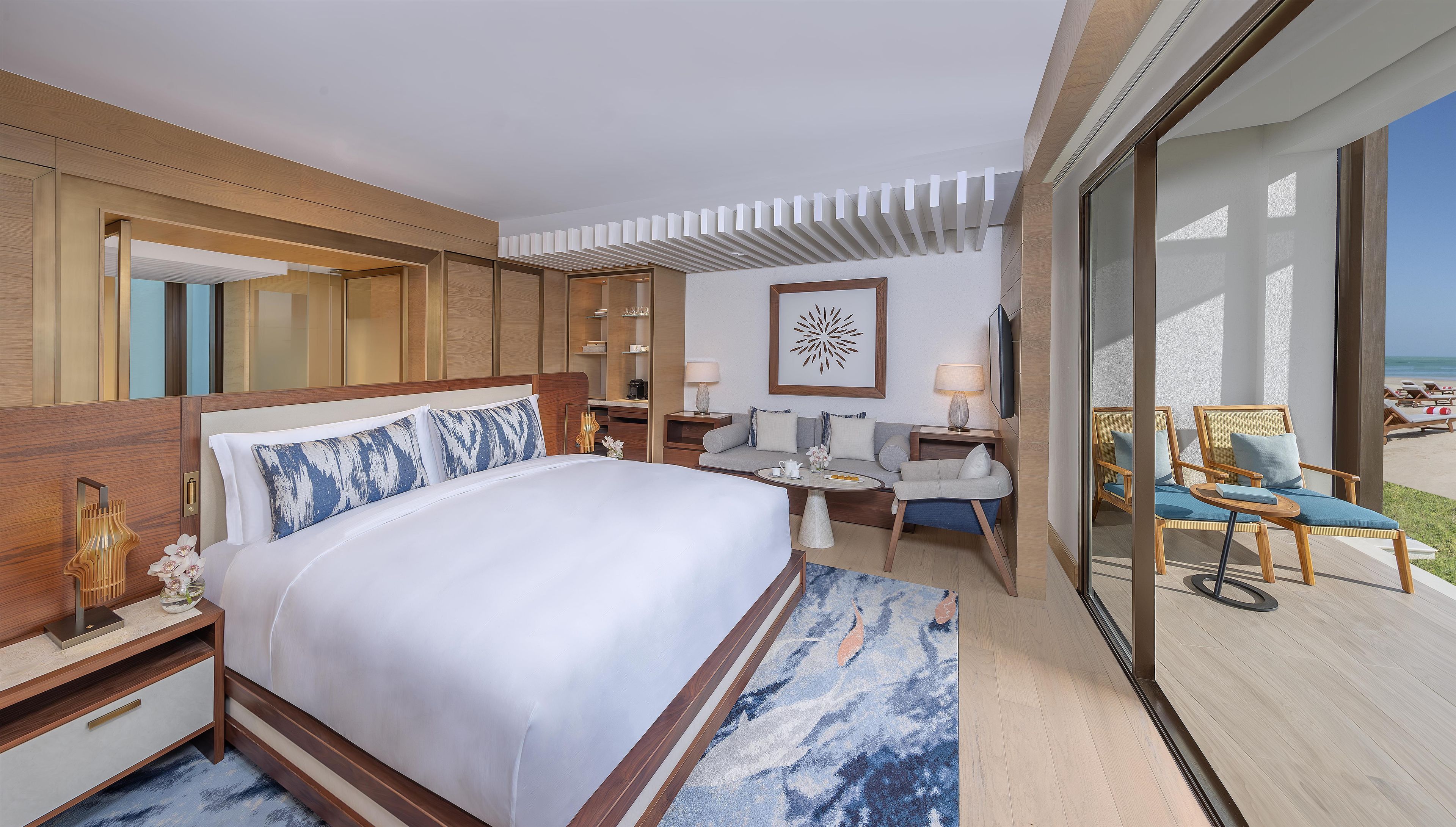 A hotel room with a large bed, a sofa, a dining table, and a view of the beach.