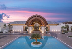 Un hotel moderno con piscina, entrada en arco y caminos bien iluminados.