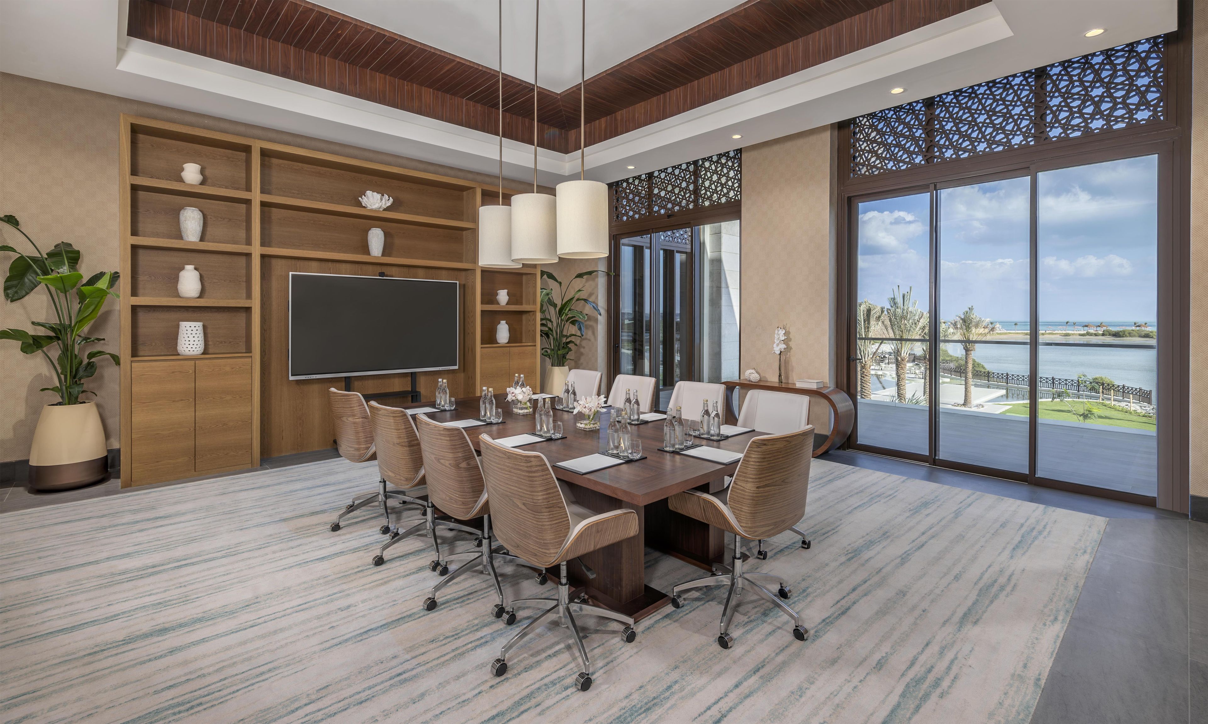 A conference room with a large table, chairs, a flat-screen TV, and a view of the sea.