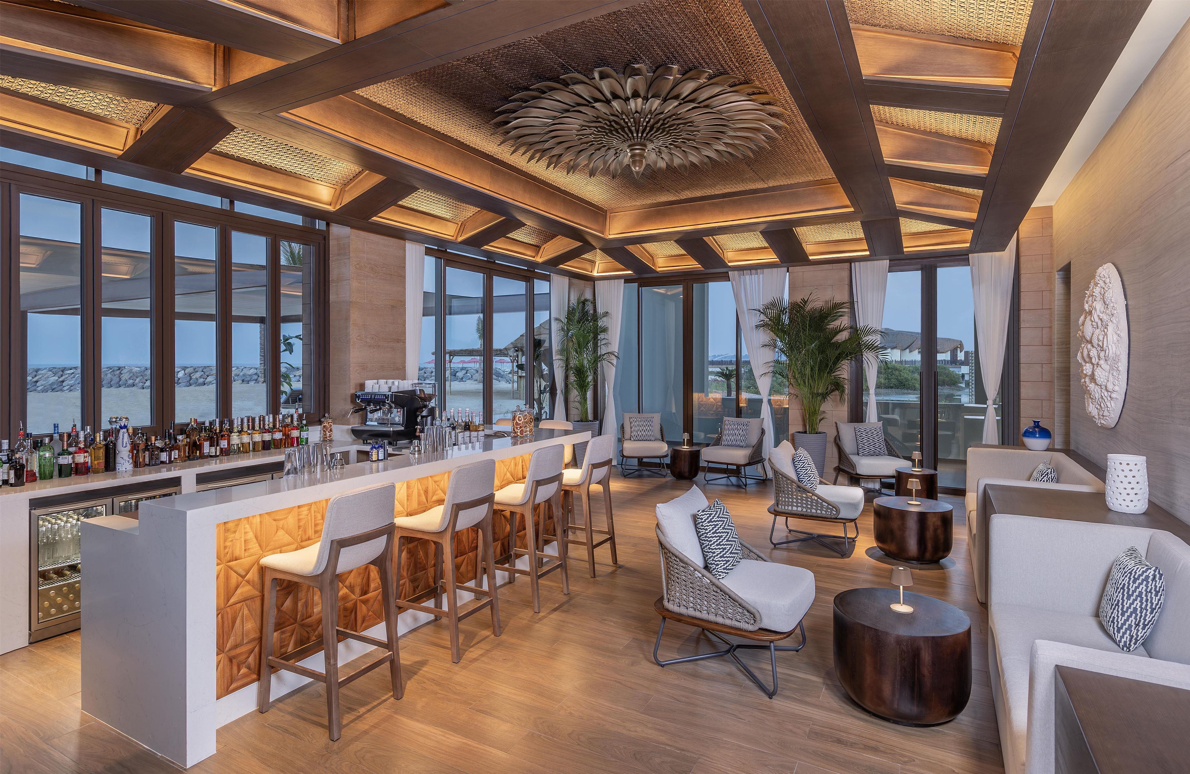 A modern bar area with a long counter, bar stools, and a view of the beach.