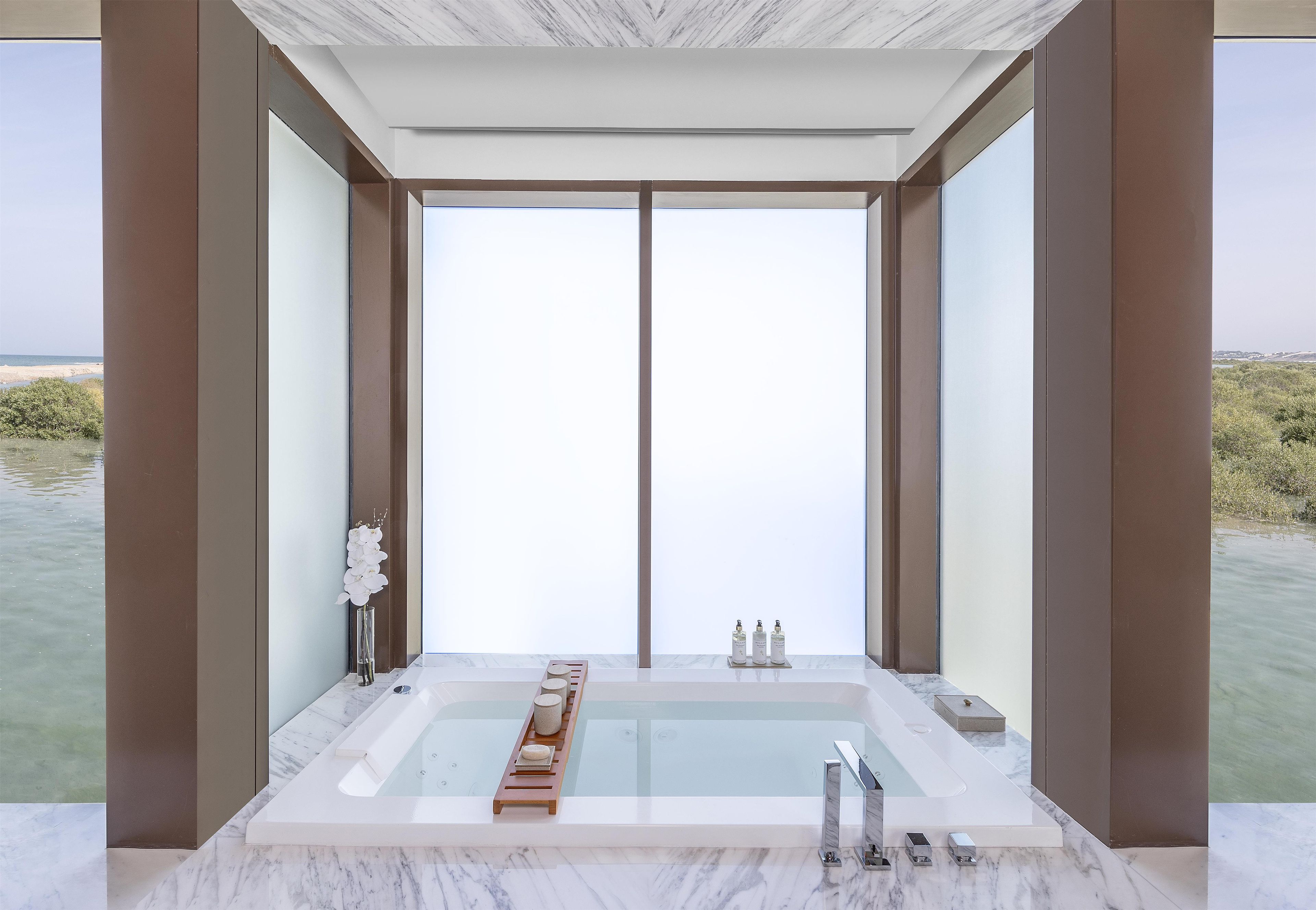 Un baño moderno con una bañera grande, suelo de mármol y vistas al mar.
