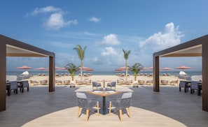 A beachside patio with outdoor seating and umbrellas, overlooking the ocean. - Anantara Mina Ras Al Khaimah Resort (Ras Al Khaimah)