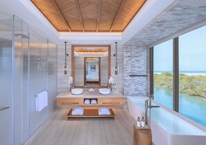 Une salle de bain moderne avec un grand miroir, deux lavabos, une baignoire et une vue sur la mer.