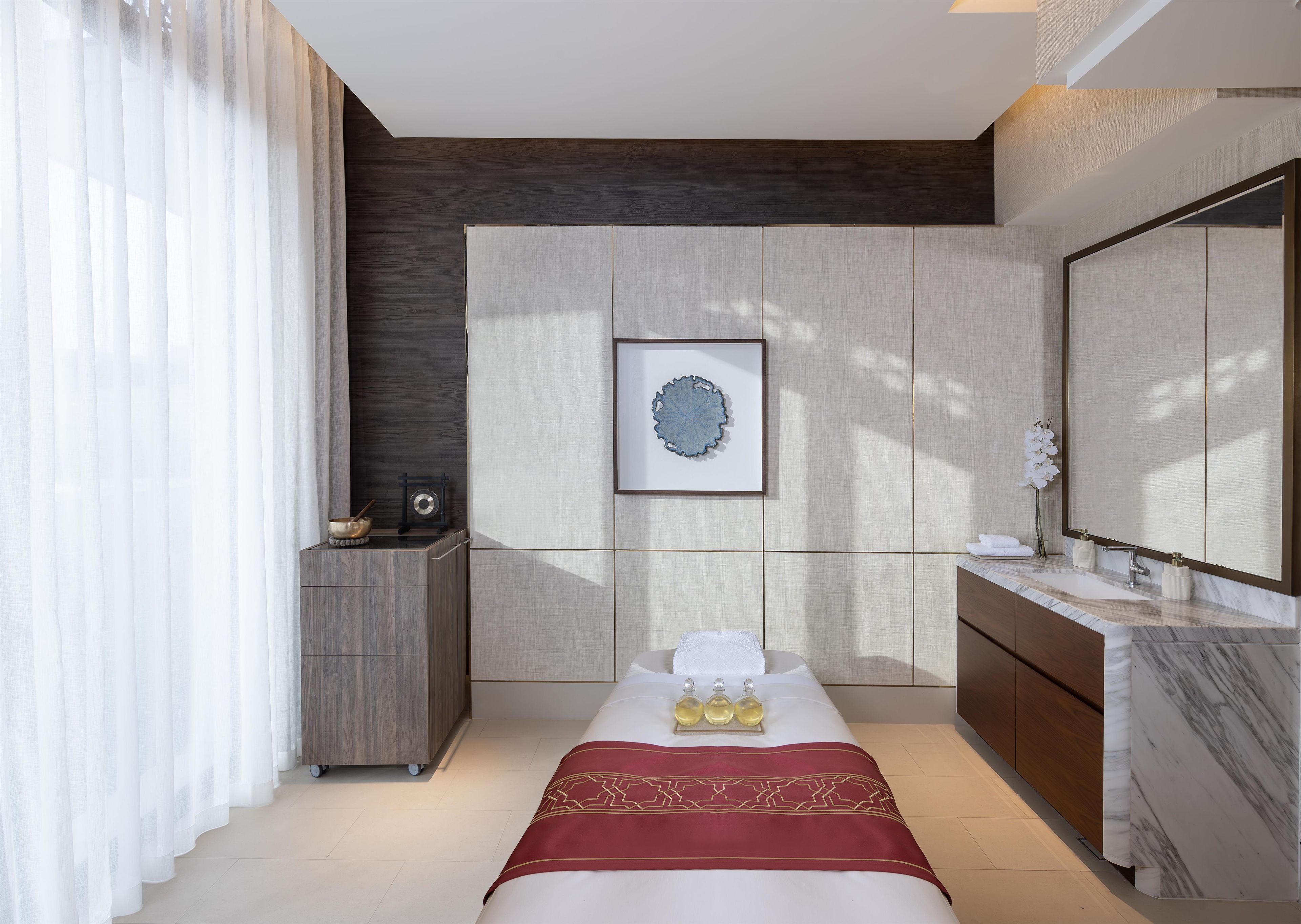 Una habitación de hotel moderna con una cama, una tocador con un espejo grande, un mueble pequeño y una obra de arte enmarcada en la pared.