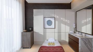 Una habitación de hotel moderna con una cama, una tocador con un espejo grande, un mueble pequeño y una obra de arte enmarcada en la pared.