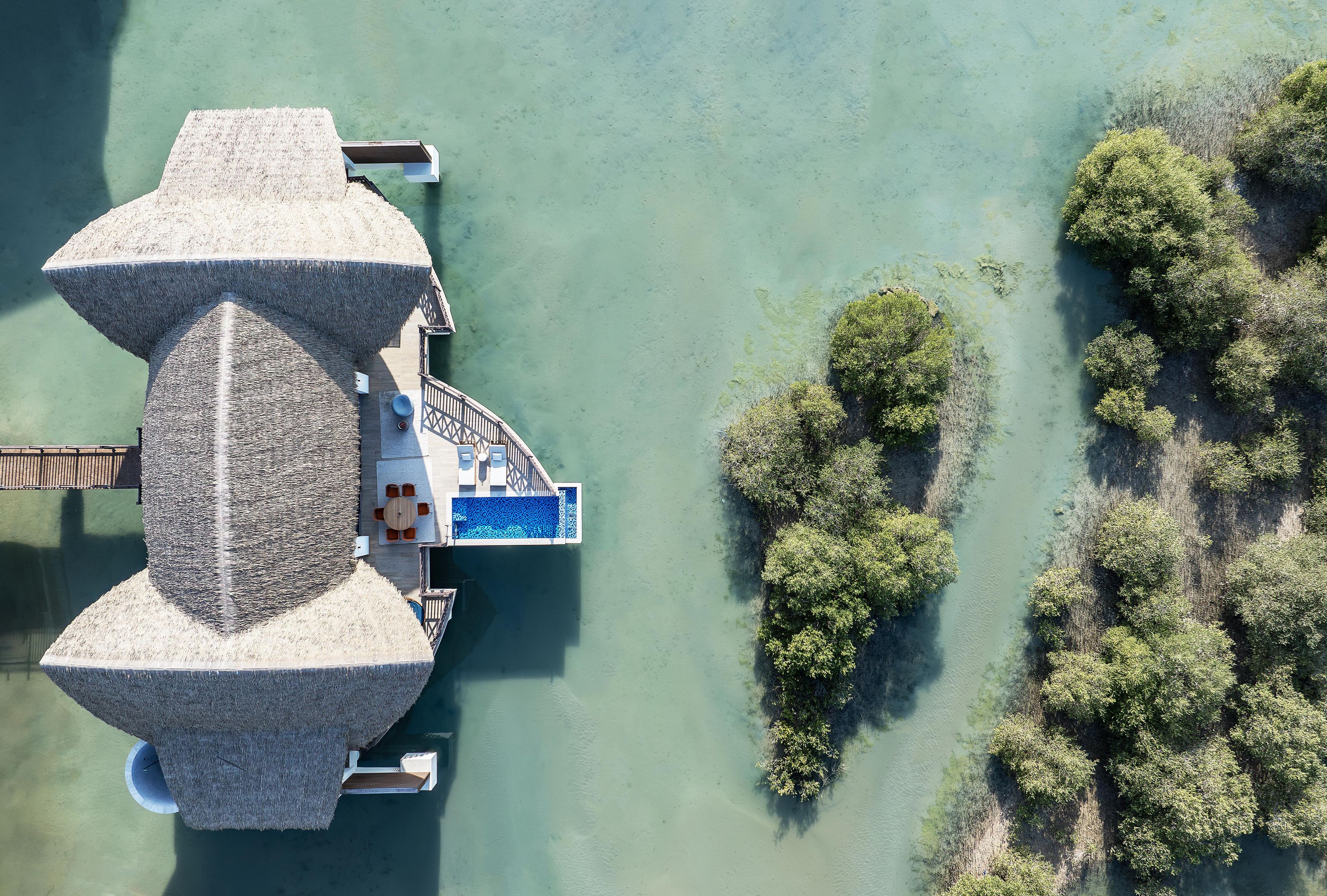 An aerial view of a resort with a large thatched structure, a pool area, and surrounding greenery.