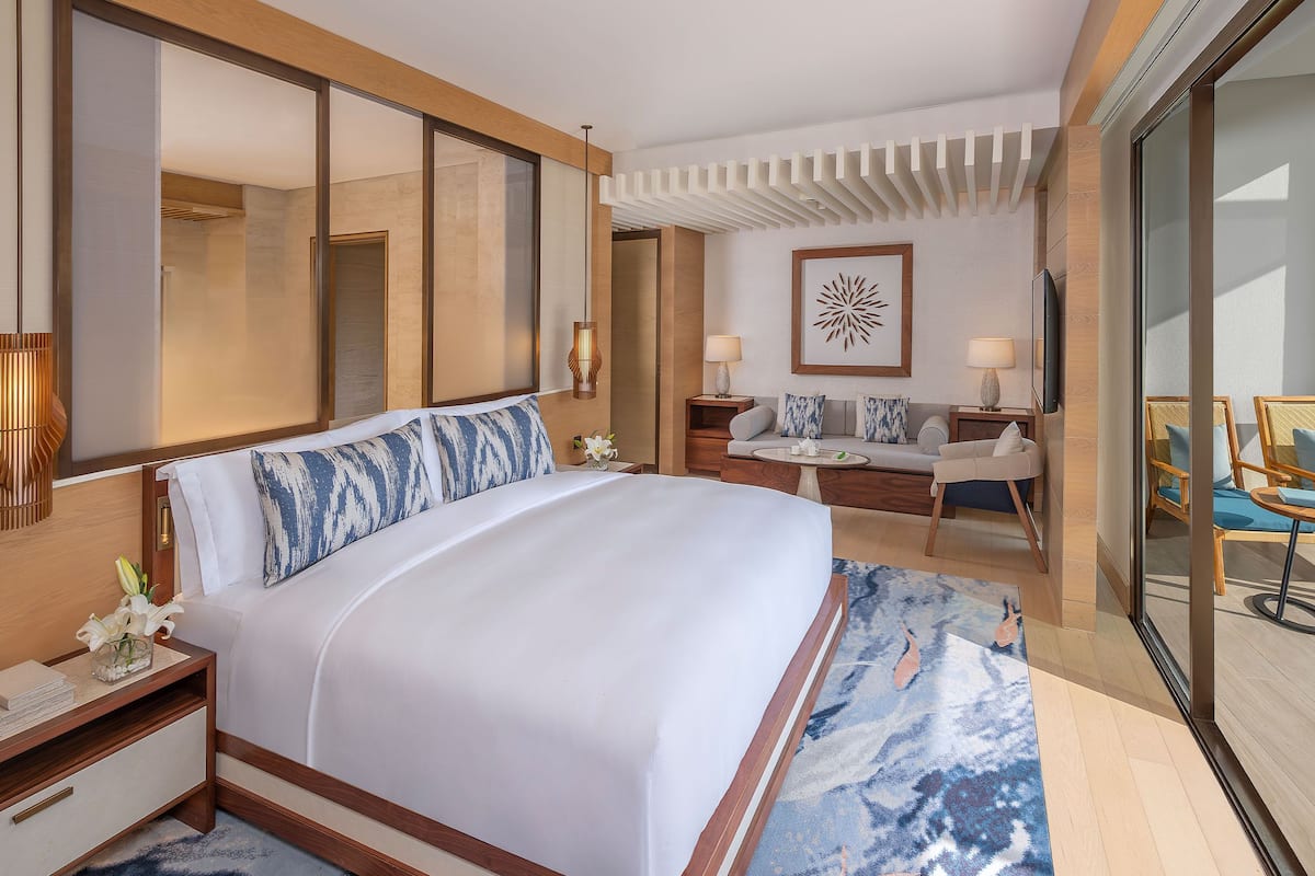 Una habitación de hotel moderna con una cama grande, un sofá, un escritorio y un balcón con mobiliario exterior.