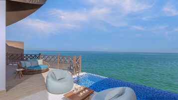 Un balcón con un sofá de mimbre, un sillón informal y una pequeña mesa con bebidas, con vistas a un mar azul y despejado.