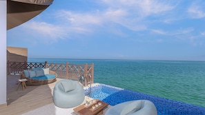 A balcony with a wicker sofa, a bean bag, and a small table with drinks, overlooking a clear blue sea. - Anantara Mina Ras Al Khaimah Resort (Ras Al Khaimah)