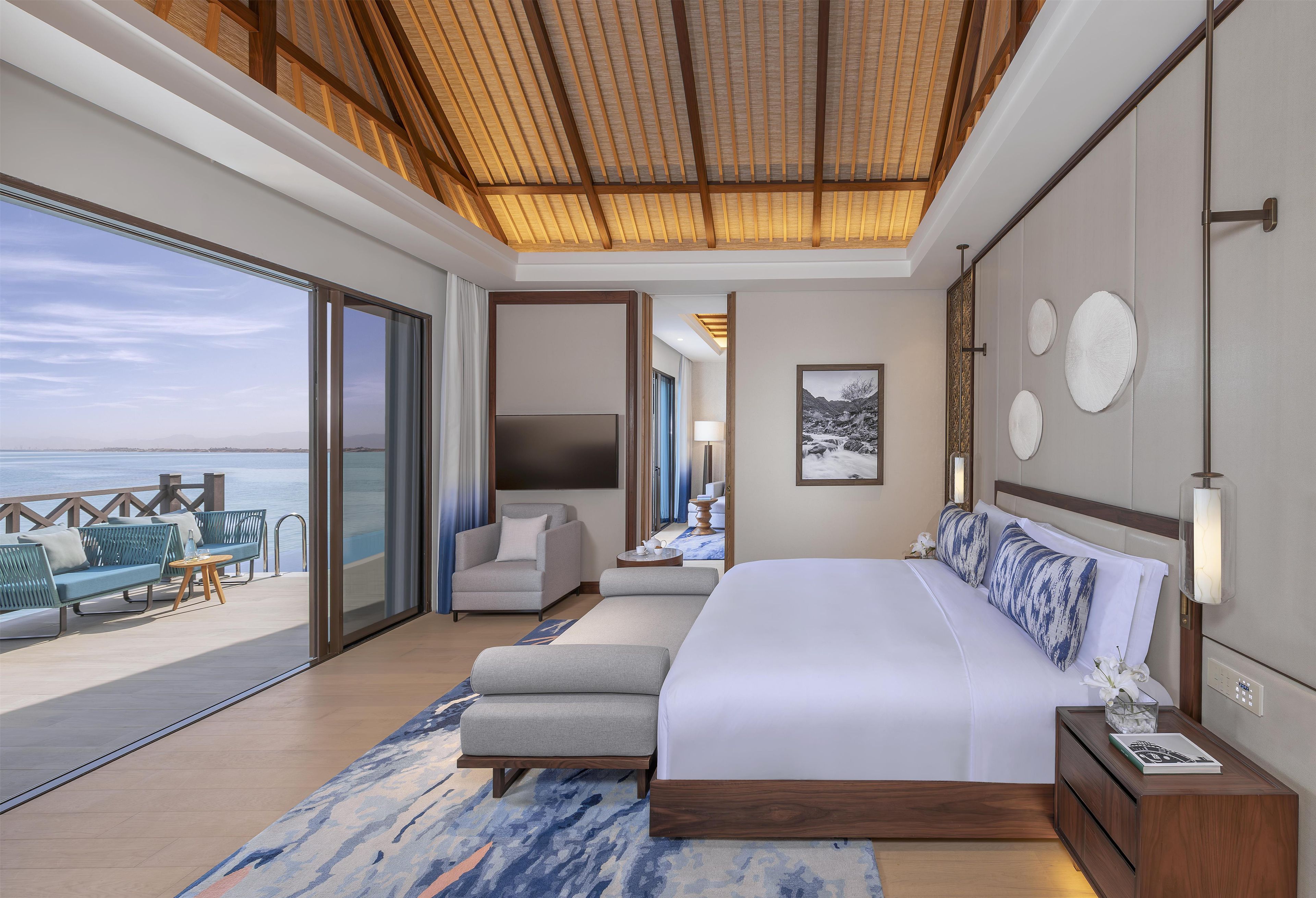 A modern hotel room with a large bed, a seating area with a view of the sea, and a balcony.