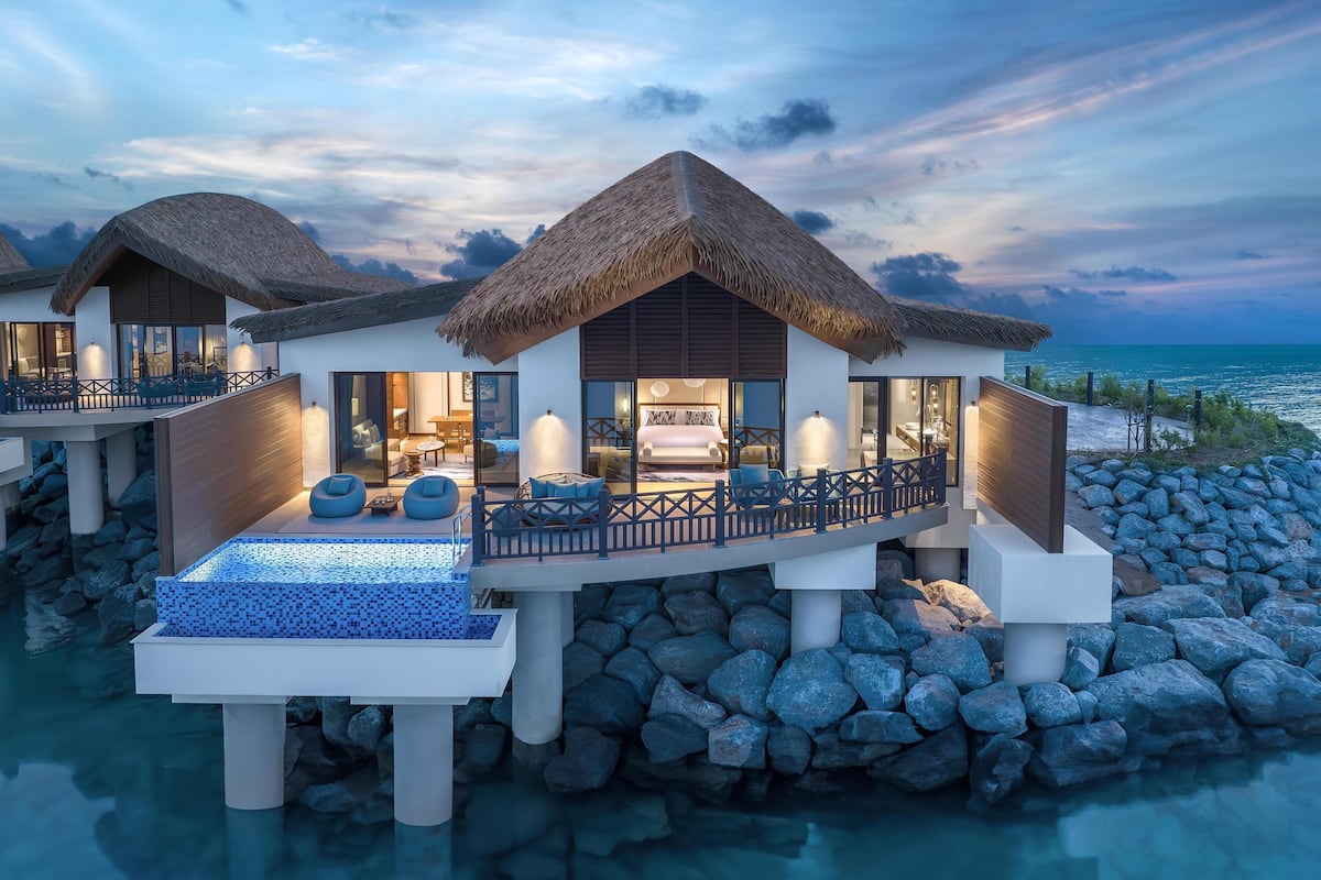 Una lujosa villa sobre el agua con techo de paja, piscina infinita privada y balcón con vistas al mar.