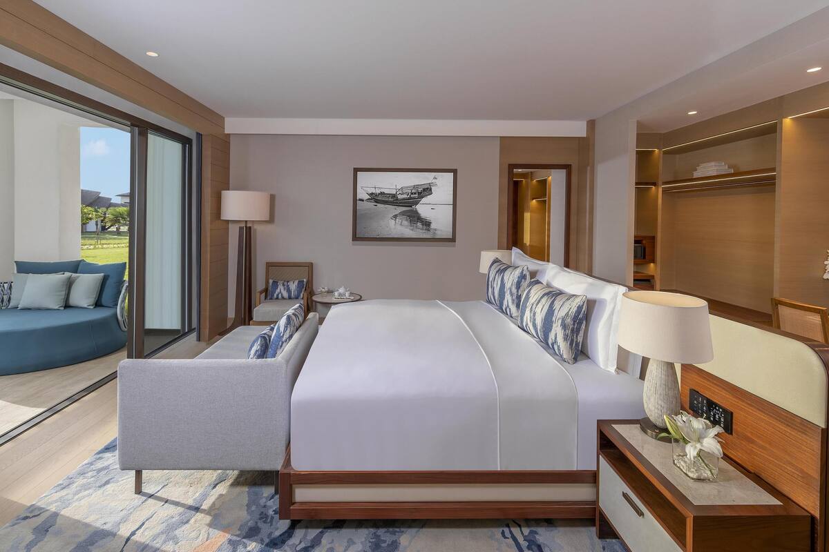 Una habitación de hotel moderna con una cama grande, una zona de estar con sofá, un escritorio y vistas al exterior.
