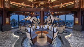 A circular seating area with a central pole, surrounded by chairs with cushions, and a view of the outdoors through large windows. - Anantara Mina Ras Al Khaimah Resort (Ras Al Khaimah)