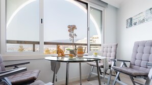 Un balcón moderno con una mesa de vidrio, dos sillas acolchadas y una planta de orquídea decorativa.