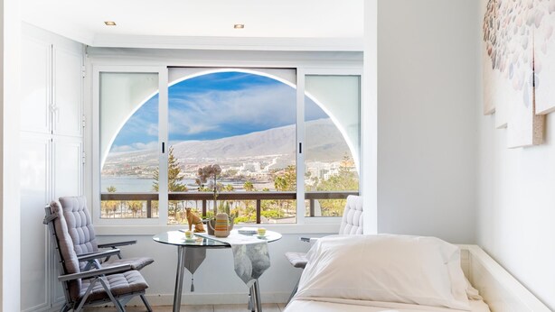 Una habitación de hotel con cama, una zona de estar con mesa, y un ventanal que ofrece una vista panorámica.