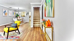 A modern living room with a yellow armchair, a colorful rug, and a staircase leading to another room.