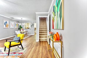Una sala moderna con un sillón amarillo, un tapete colorido y una escalera que lleva a otra habitación.