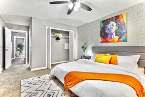 Une chambre à coucher avec un lit, un ventilateur de plafond, un tableau et un tapis à motifs géométriques.