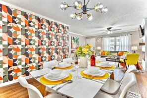 Une salle à manger avec un papier peint à motifs géométriques, un lustre et une table à manger dressée pour six personnes, agrémentée de sets de table jaunes.