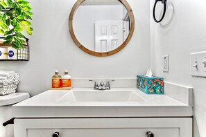 Une salle de bain avec un lavabo blanc, un miroir rond, un porte-serviettes et une plante en pot.