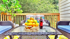 An outdoor patio with wicker furniture, a glass table, a fruit basket, and a bottle of wine.