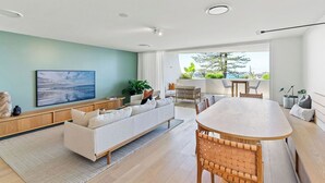 Ein modernes Wohnzimmer mit einer Couch, einem Esstisch und Stühlen. Ein großes Fenster bietet Blick auf grüne Vegetation draußen.