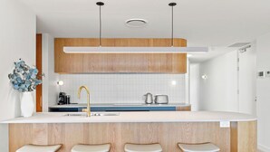 Eine moderne Küche mit Holzausstattung, einer weißen Arbeitsplatte, einer zentralen Kochinsel mit Hockern und Pendelleuchten.