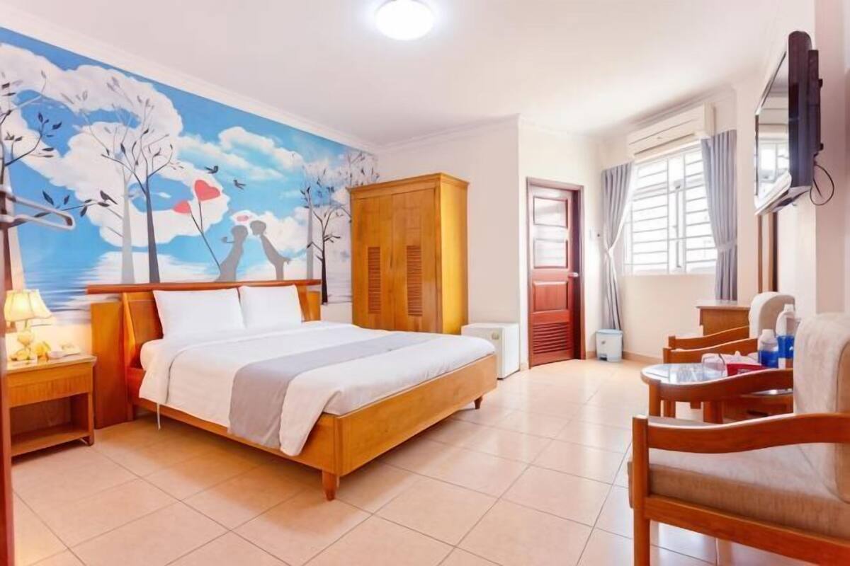 A bedroom with a bed, wooden wardrobe, bedside table, and a mural on the wall.