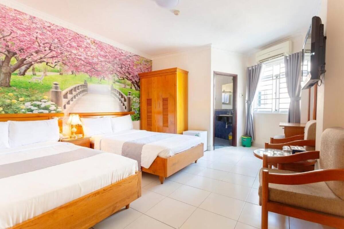 A hotel room with two beds, a wooden wardrobe, a TV, and a view of a cherry blossom tree through a window.