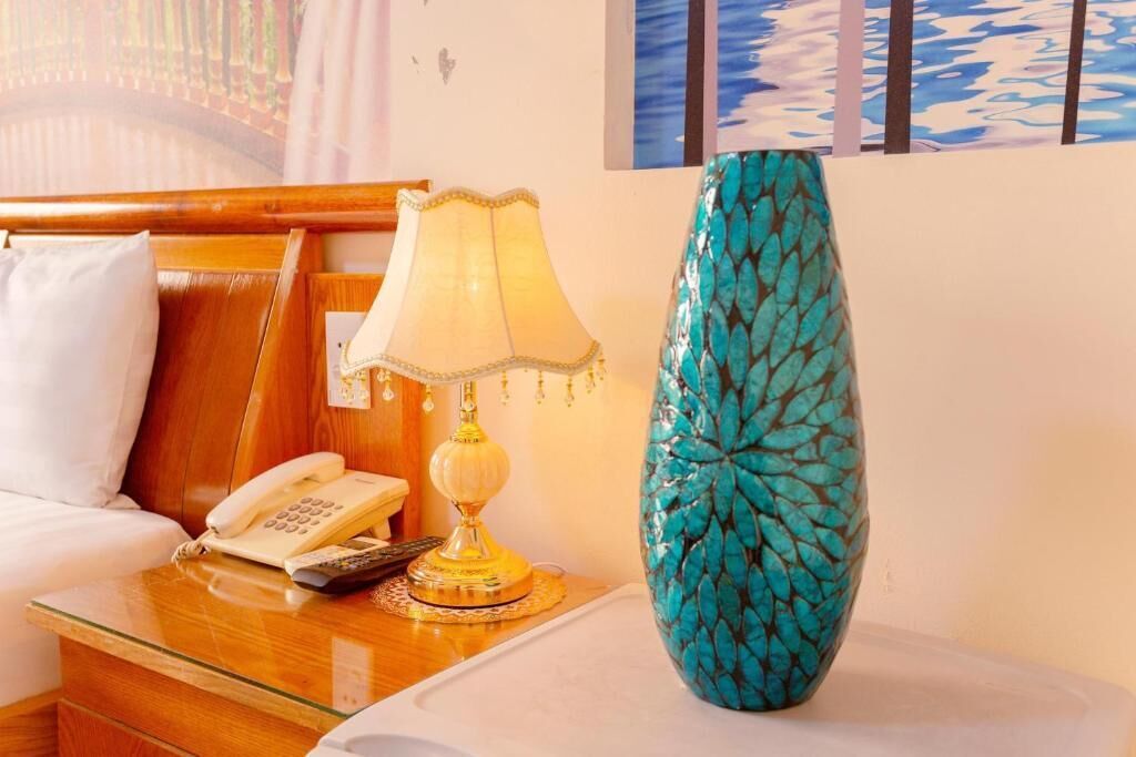 A hotel room with a wooden headboard, a bedside lamp, a telephone, and a turquoise vase on a table.